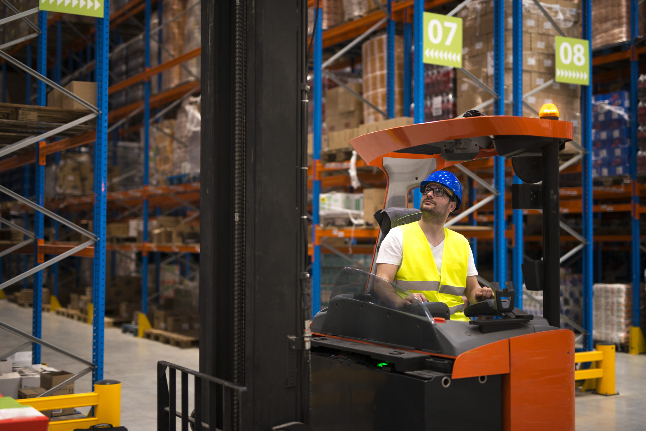 Forklift driver relocating and lifting goods in large warehouse