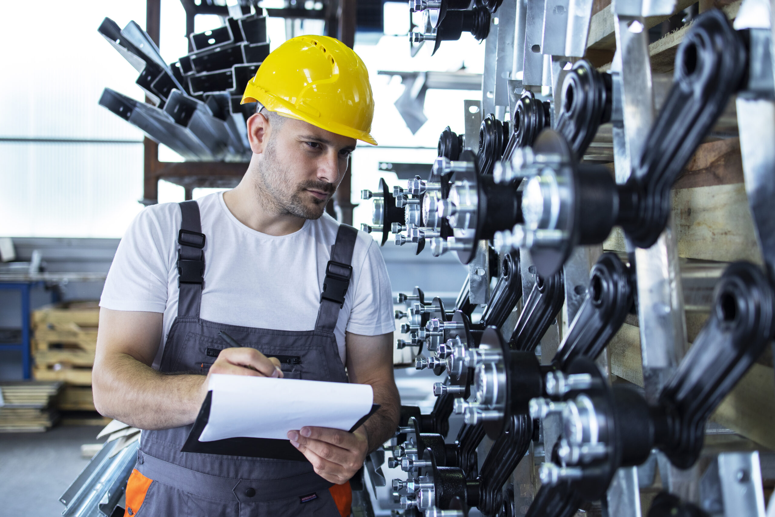 Industrial employee wearing uniform and yellow hardhat checking production in factory.